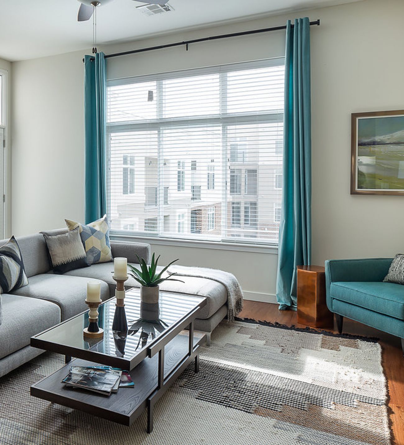 Domain City Center A modern living room features a gray sectional sofa with blue and gray pillows, a teal armchair, and a large abstract art piece on the wall.